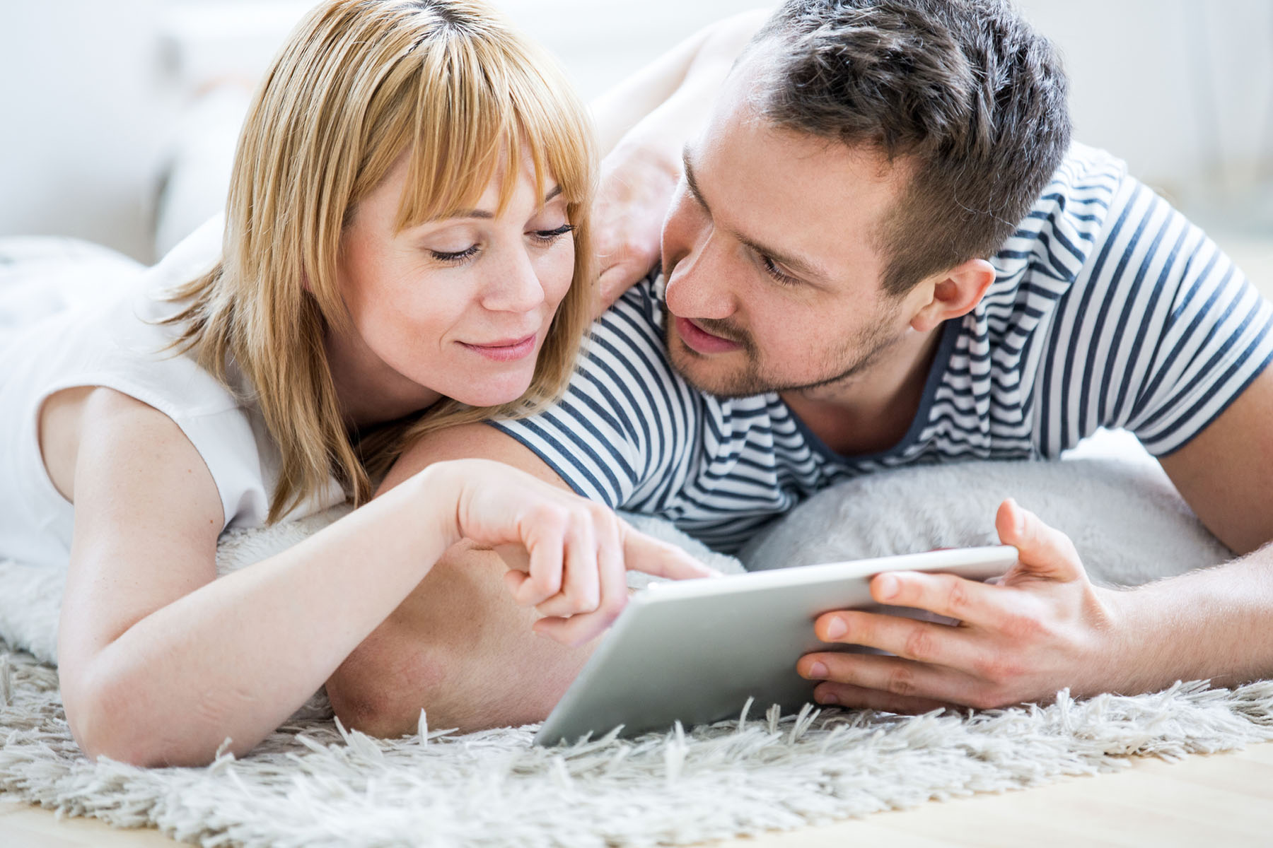 Couple with tablet lying on carpet